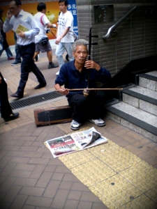 An old man playing a string instrument outside Wan Chai Station